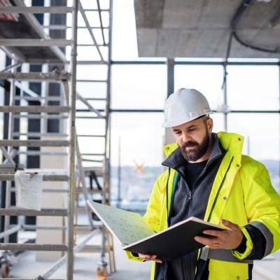 Mature man engineer standing on construction site, holding blueprints.